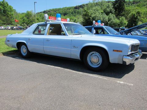 1991 Ford LTD Crown Victoria - light-blue 1970s State Police sedan with twin roof beacons and a red State Police roof sign, parked on a lot.