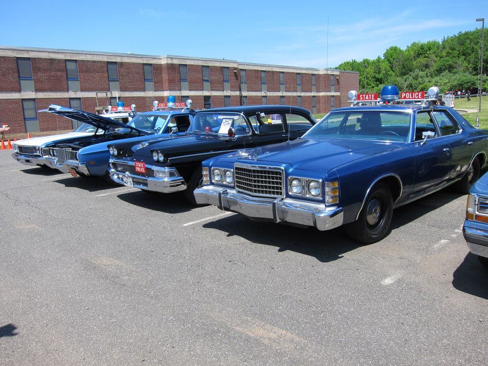 Row of vintage 1970s blue Ford police sedans parked in front of a brick building
