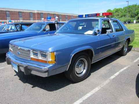1991 Ford LTD Crown Victoria - light blue Ford LTD Crown Victoria four-door police sedan with a red and blue roof light bar parked on asphalt.