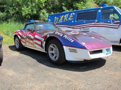 1991 Ford LTD Crown Victoria - patriotic flag-painted Connecticut State Police Corvette with blue light bar parked next to a blue D.A.R.E. van.