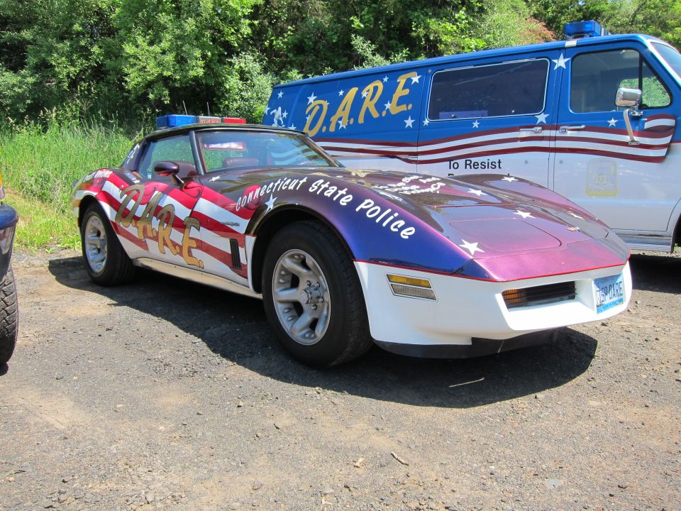 Connecticut State Police flag-painted Corvette beside a blue D.A.R.E. van