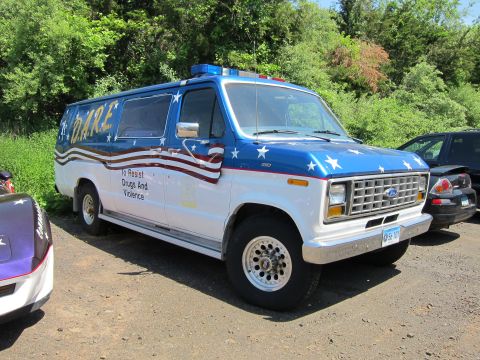 1991 Ford LTD Crown Victoria - white and blue Ford van painted with stars and stripes and D.A.R.E. To Resist Drugs And Violence lettering on a dirt lot.