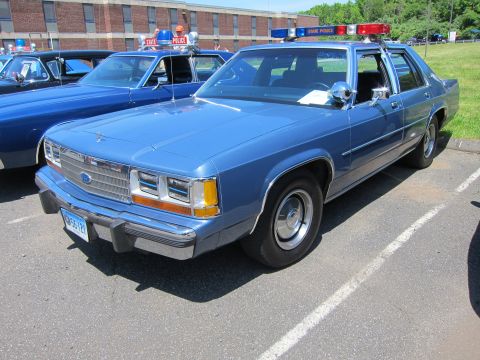1991 Ford LTD Crown Victoria - light blue Ford LTD Crown Victoria four-door police sedan with a roof light bar parked on grass at an outdoor show.