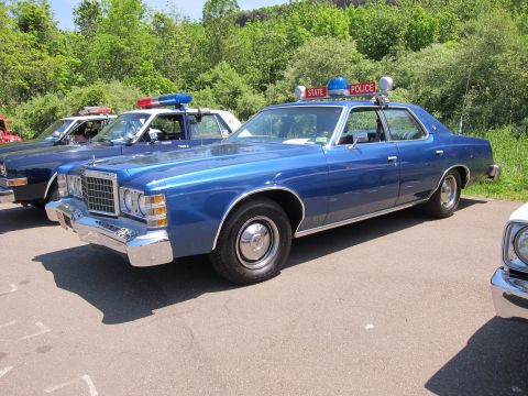 1991 Ford LTD Crown Victoria - blue 1970s Ford LTD full-size sedan lettered STATE POLICE with red and blue roof lights parked at an outdoor show.