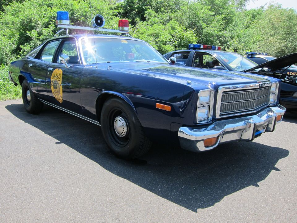 Dark blue 1970s Plymouth police sedan with gold door seal and roof lights