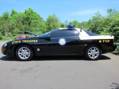 1991 Ford LTD Crown Victoria - Side view of a black and tan Chevrolet Camaro state trooper car lettered FHP with hood raised, blue roof light bar.