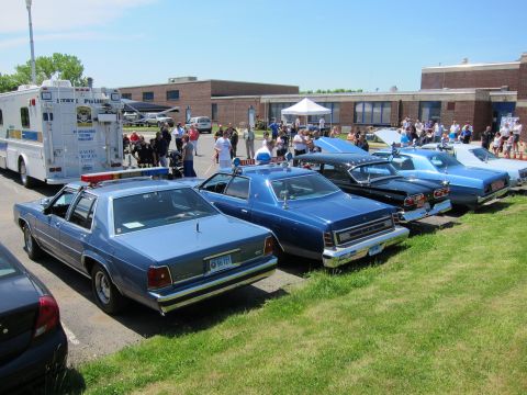 1991 Ford LTD Crown Victoria - lineup of blue police sedans and classic cars parked on grass beside a State Police box truck with a crowd behind.