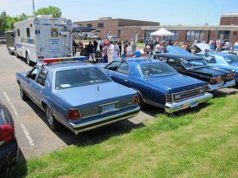1991 Ford LTD Crown Victoria - Rear view of a row of police sedans, including a blue Ford, parked on grass beside a command box truck with spectators.