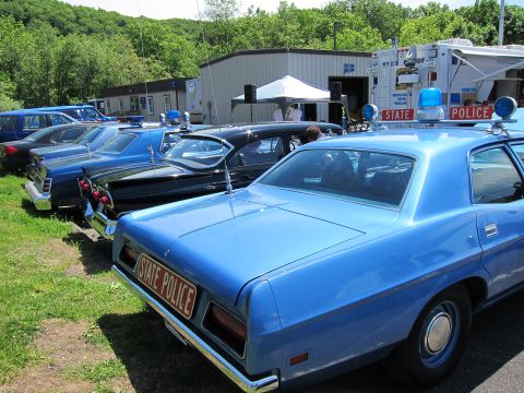 1991 Ford LTD Crown Victoria - blue classic State Police sedan with trunk lettering sits at the front of a row of vintage police cruisers at an outdoor gathering.