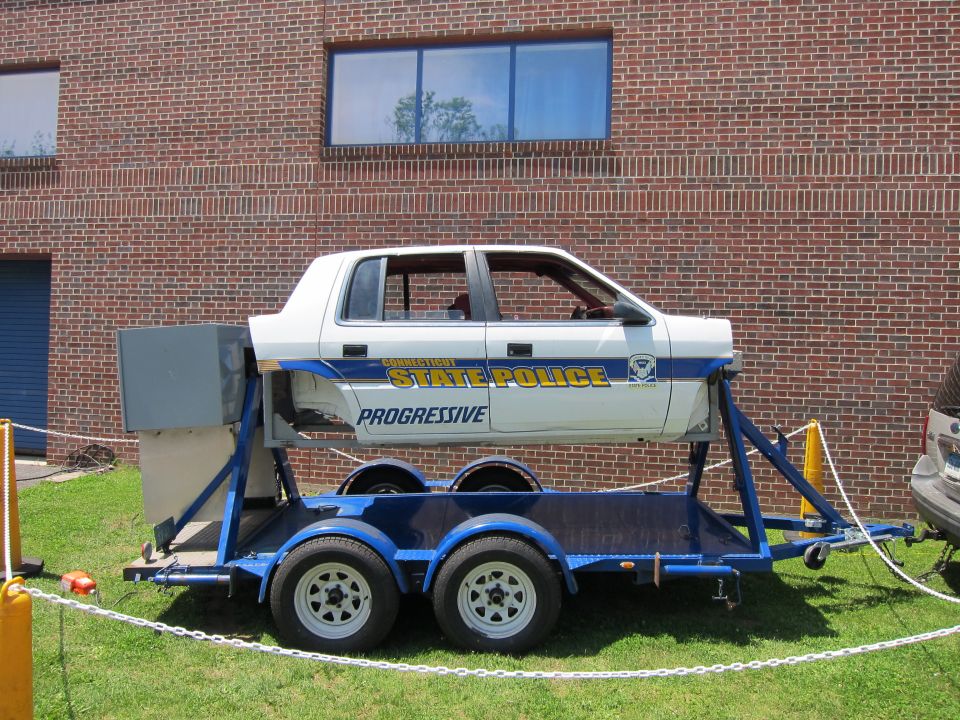 White Connecticut State Police car body mounted on a blue rollover trailer