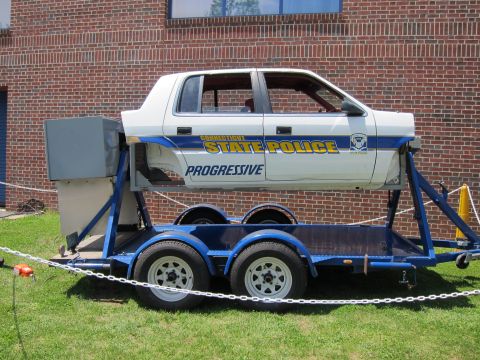 1991 Ford LTD Crown Victoria - Side view of a white Connecticut State Police car shell labeled Progressive mounted on a blue tandem-axle demonstration trailer.