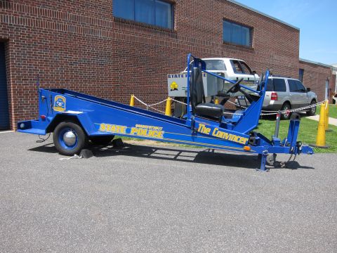 1991 Ford LTD Crown Victoria - Full side view of a long blue Connecticut State Police seatbelt convincer ramp trailer parked in a paved lot by a brick building.