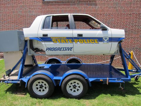 1991 Ford LTD Crown Victoria - Side view of a white-and-blue Connecticut State Police rollover-demonstration car body marked Progressive on a blue trailer.