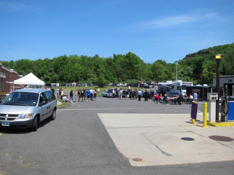 1991 Ford LTD Crown Victoria - wide view of an outdoor event with a silver Dodge minivan, scattered crowd, white tent, and a large RV under a blue sky.