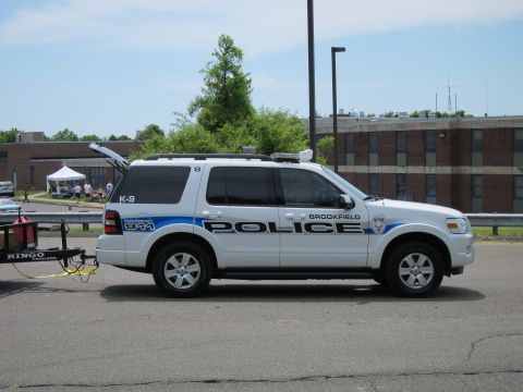 1991 Ford LTD Crown Victoria - white Ford Explorer marked Brookfield Police K-9 with blue striping parked on pavement beside a brick building.