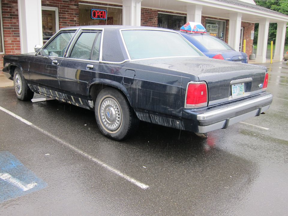 Dark sedan parked in a wet lot, rear view. License plate reads 327-7457