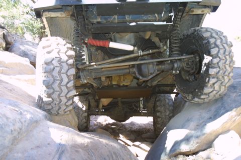 1994 Ford Bronco - The undercarriage of an off-road vehicle is visible as it maneuvers over large rocks, highlighting its suspension and tires.