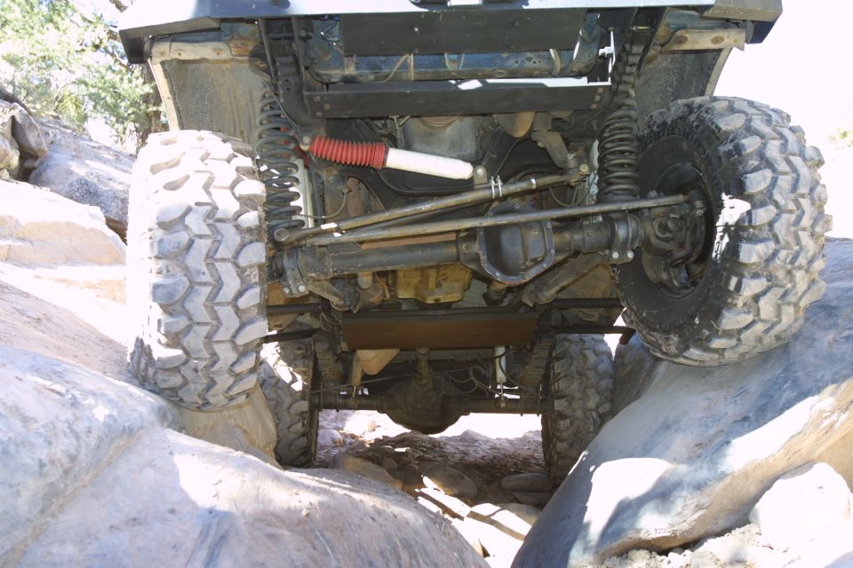 Undercarriage of lifted 4x4 crawling over boulders, showing front axle and suspension