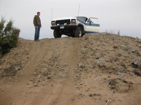1979 Ford Bronco - A man stands next to a white and blue 1979 Ford Bronco parked on a dirt hill, with the driver's door open.