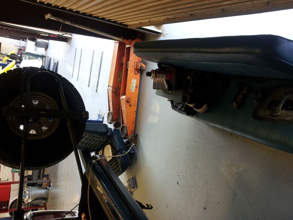 Spare tire mounted on a rack inside a vehicle, with a blue seat and orange machinery visible
