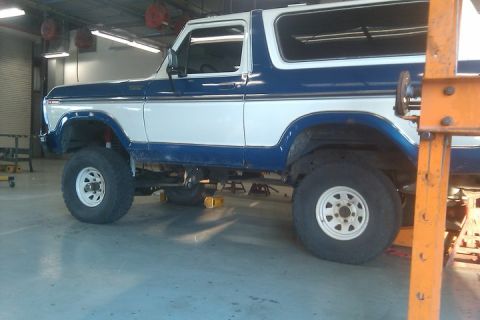 1979 Ford Bronco - This two-tone Ford Bronco is raised on hydraulic lifts inside a workshop.