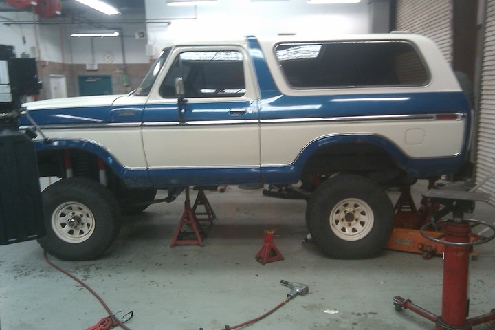 1978 Ford Bronco lifted on jack stands in a garage, undergoing maintenance