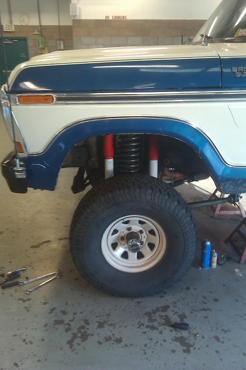 1979 Ford Bronco - The front quarter panel and wheel of a lifted Ford Bronco are visible, with tools on the floor.