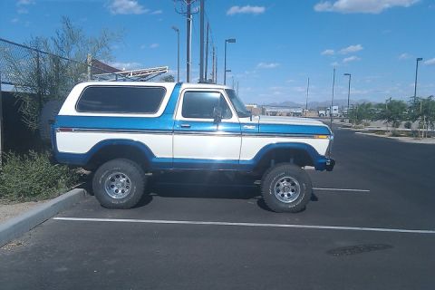 1979 Ford Bronco - A two-tone white and blue Ford Bronco is parked in a lot under a bright blue sky.