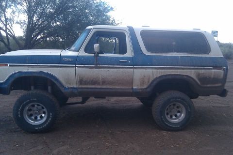 1979 Ford Bronco - A lifted, two-tone blue and white Ford Bronco sits on a dirt road.