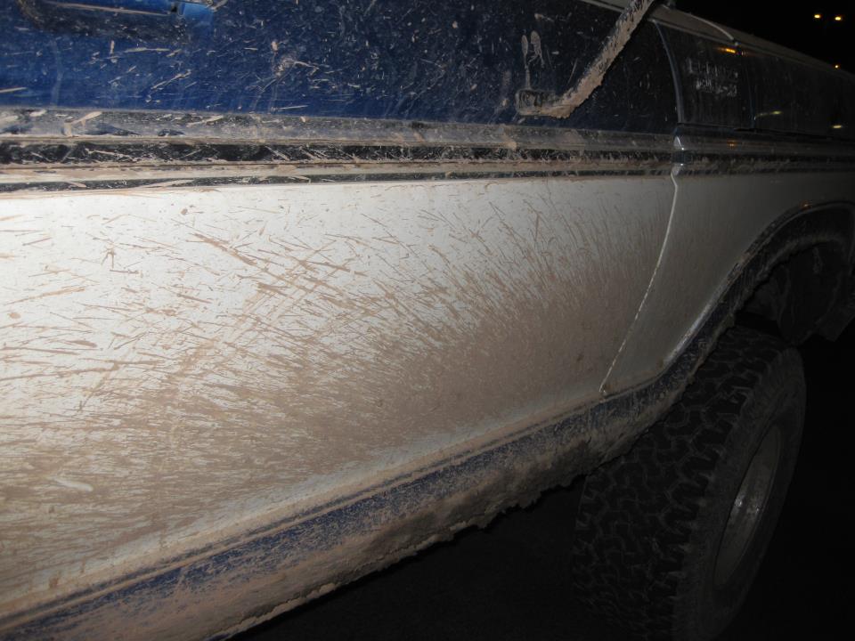 Mud-splattered side of a 1979 Ford Bronco, white and blue two-tone paint