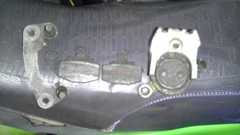 1989 Ford Bronco - A brake caliper and two brake pads are displayed on a dark, textured surface.