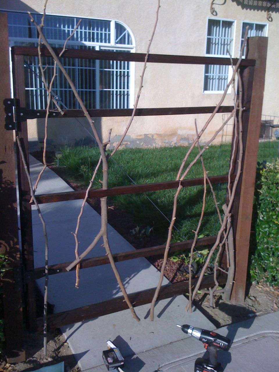 Wooden gate with branches, concrete path, and a drill