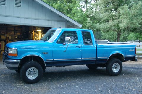 1992 Ford F-150 - A bright blue 1990s Ford F-150 extended-cab pickup shown in full side profile, lifted on chrome/machined wheels with all-terrain tires, a d…