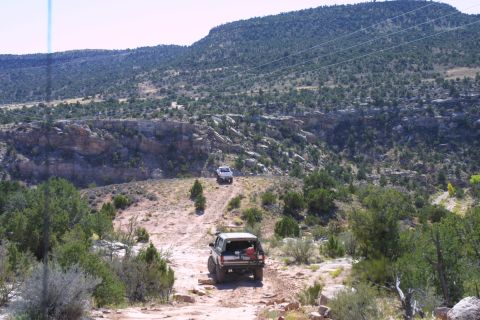 1994 Ford Bronco - Two SUVs navigate a off-road trail through a rocky, arid landscape under a clear sky.