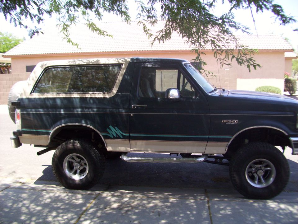 Side view of a 1993 Ford Bronco, dark green with tan trim and a spare tire