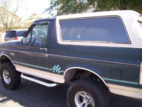 1993 Ford Bronco - Side view of a dark green 1993 Ford Bronco with a white removable top and teal accent stripe.