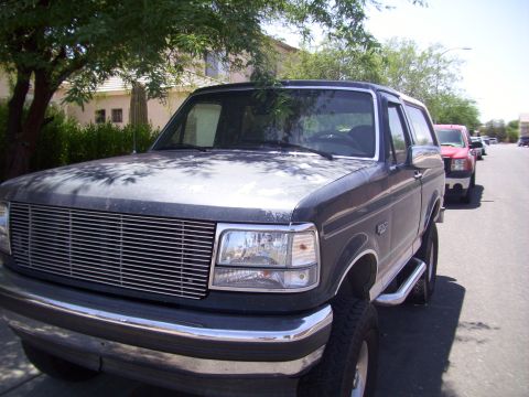 1993 Ford Bronco - A dark gray Ford Bronco is parked on the street, with another red SUV behind it.