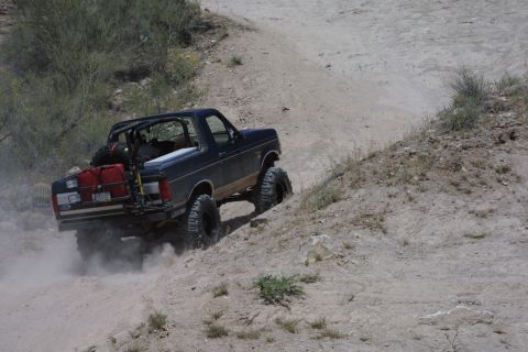 1994 Ford Bronco - A modified Ford Bronco navigates a dusty off-road path, kicking up dust as it climbs.