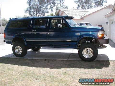 1993 Ford Bronco - This lifted blue Ford SUV is parked on a concrete driveway in front of a house.