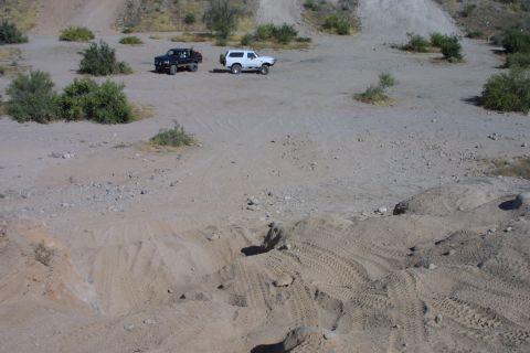 1994 Ford Bronco - Two off-road vehicles are parked in a dusty, open area with hills in the background.