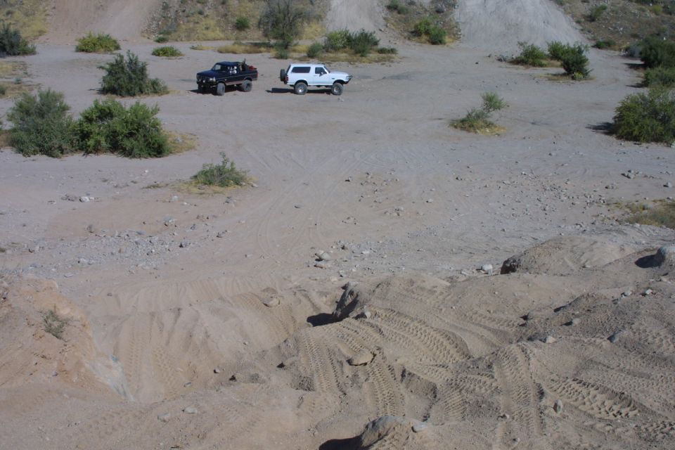 Blue and white full-size Broncos parked in a desert wash with tire tracks in the sand