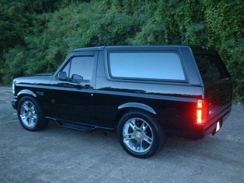 1993 Ford Bronco - This black Ford Bronco, likely a 1992 model, is shown from a rear three-quarter perspective against a backdrop of trees.