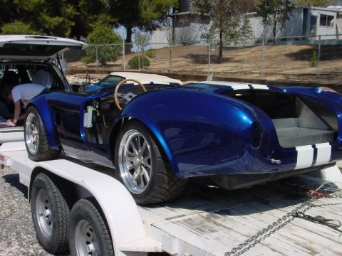 1993 Ford Bronco - A blue sports car with white racing stripes is being transported on a trailer.