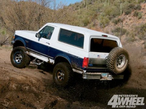 1993 Ford Bronco - This Ford Bronco is navigating a challenging off-road trail, kicking up dirt as it climbs.
