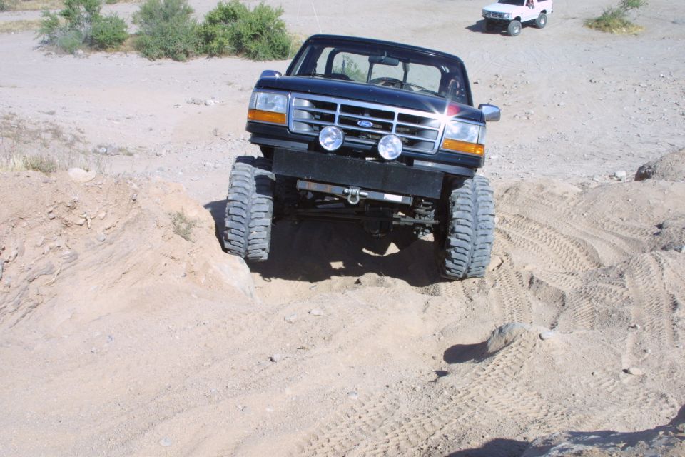 Lifted black Ford SUV front view flexing over desert sand berm on mud tires