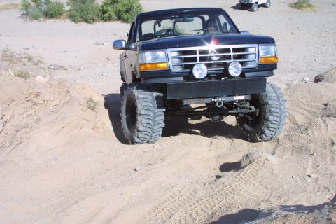 1994 Ford Bronco - A modified black Ford Bronco navigates a sandy incline, with another vehicle visible in the background.