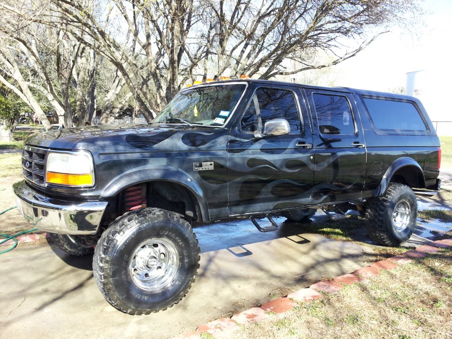 Black lifted Ford F-250/350 with flame graphics. It has large off-road tires and a raised suspension