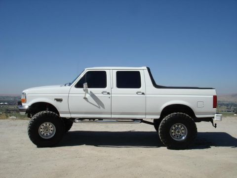1993 Ford Bronco - This lifted, white crew cab pickup truck features oversized tires and a lifted suspension, giving it an aggressive stance.