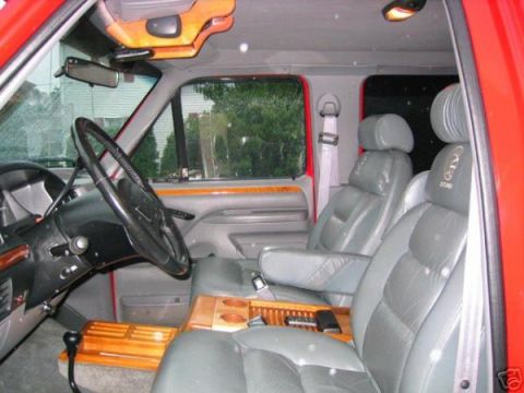 1993 Ford Bronco - Red truck cab with gray leather bucket seats, wood-grain console and door trim, shot from the passenger side.