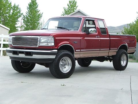 1993 Ford Bronco - This red Ford F-150 pickup truck displays a chrome grille and bumper, with a two-tone tan lower body and lifted suspension.